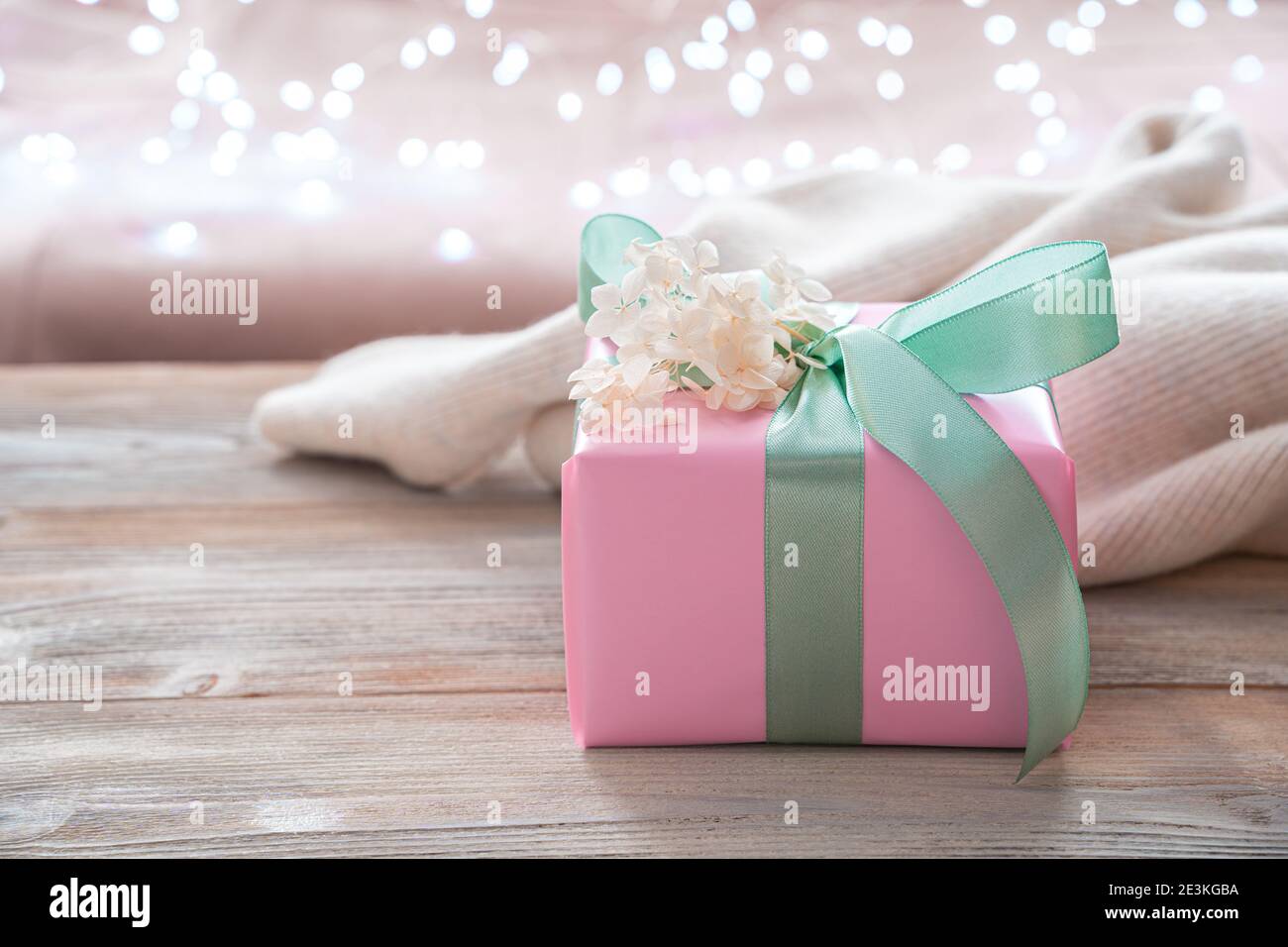 Rosa Geschenkbox mit hellgrünem Band auf hellem Hintergrund mit Girlande-Leuchten. Seitenansicht, mit Platz zum Kopieren. Stockfoto