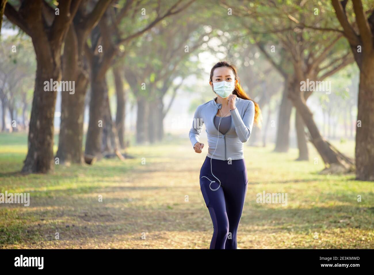 Junge Frau in Gesichtsmaske und läuft im Park Stockfoto