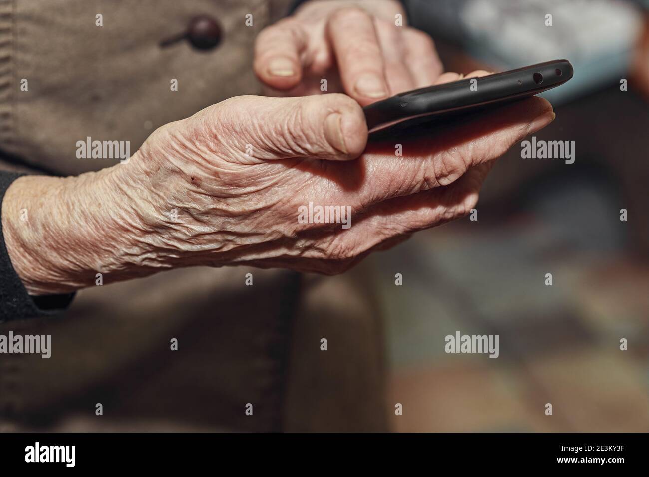 Die faltigen Hände der alten Frau halten ein modernes Mobiltelefon Stockfoto