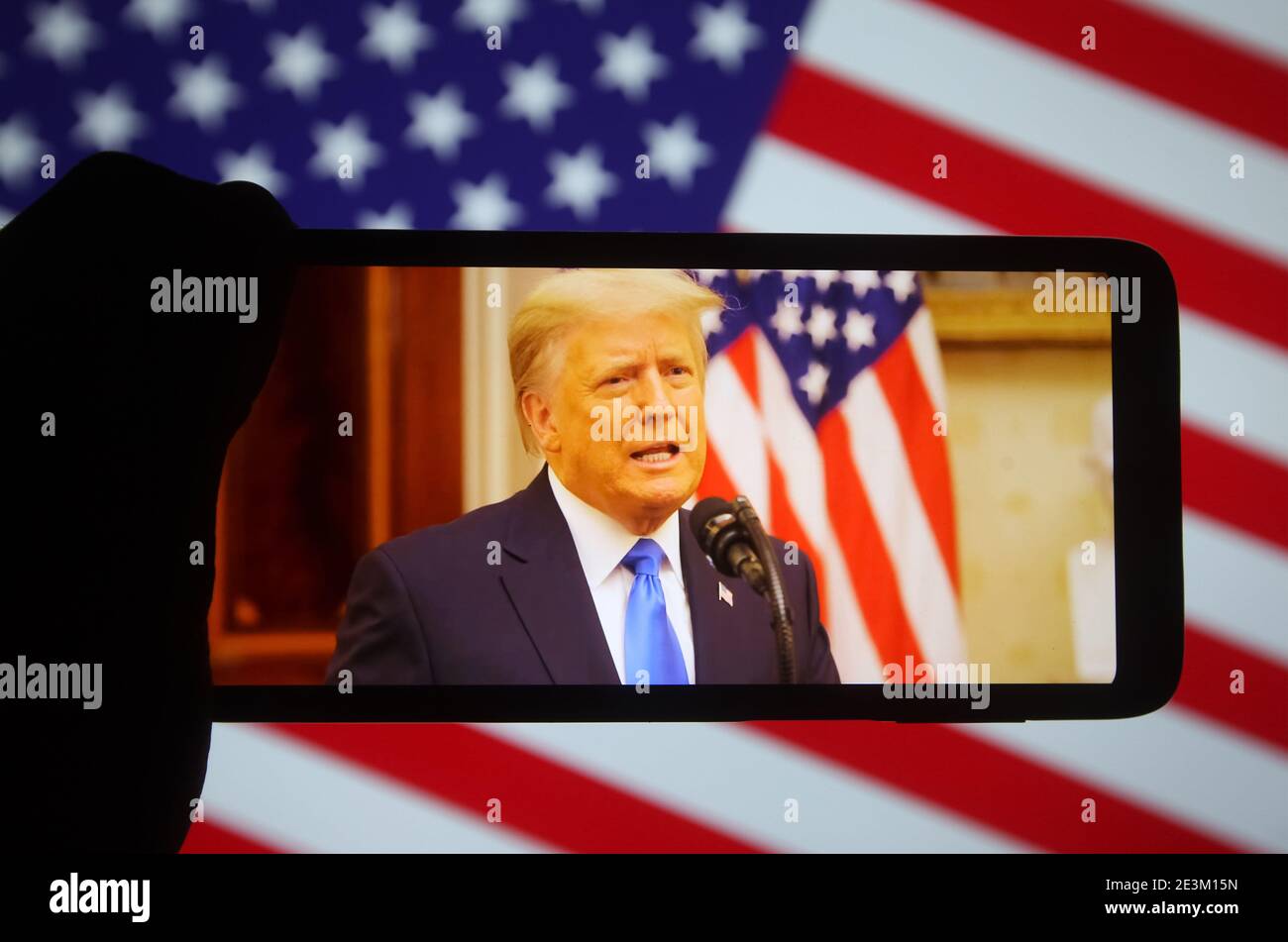 In dieser Fototafel spricht US-Präsident Donald Trump bei seiner Abschiedsrede an seinem letzten Tag im Amt auf einem Fragment von youtube-Video, das auf einem Mobiltelefon mit der US-Flagge im Hintergrund angezeigt wird. Stockfoto