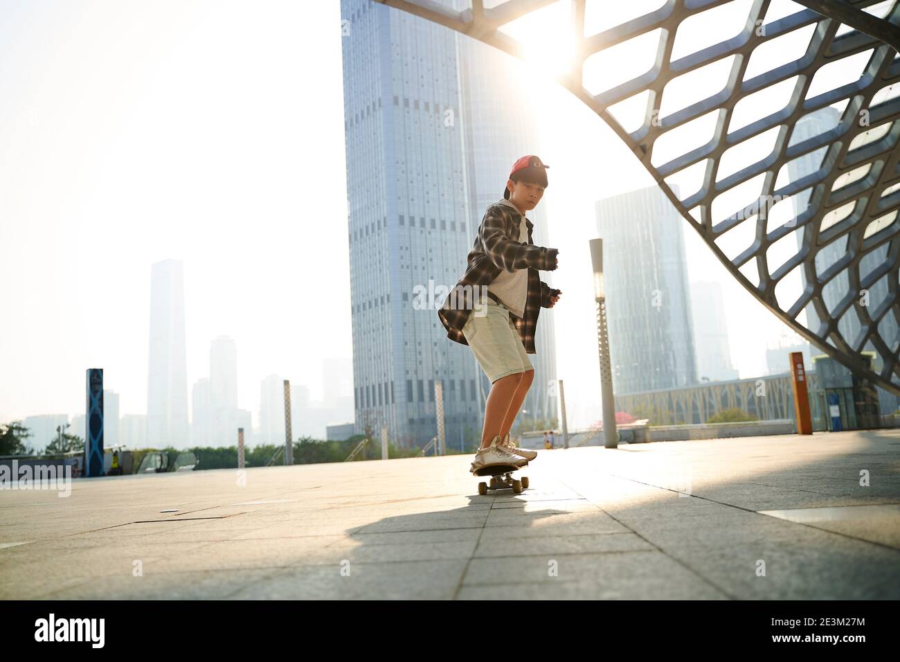 Teenager asiatische Kind Skateboarding im Freien auf Stadtplatz mit modernen Gebäude im Hintergrund Stockfoto