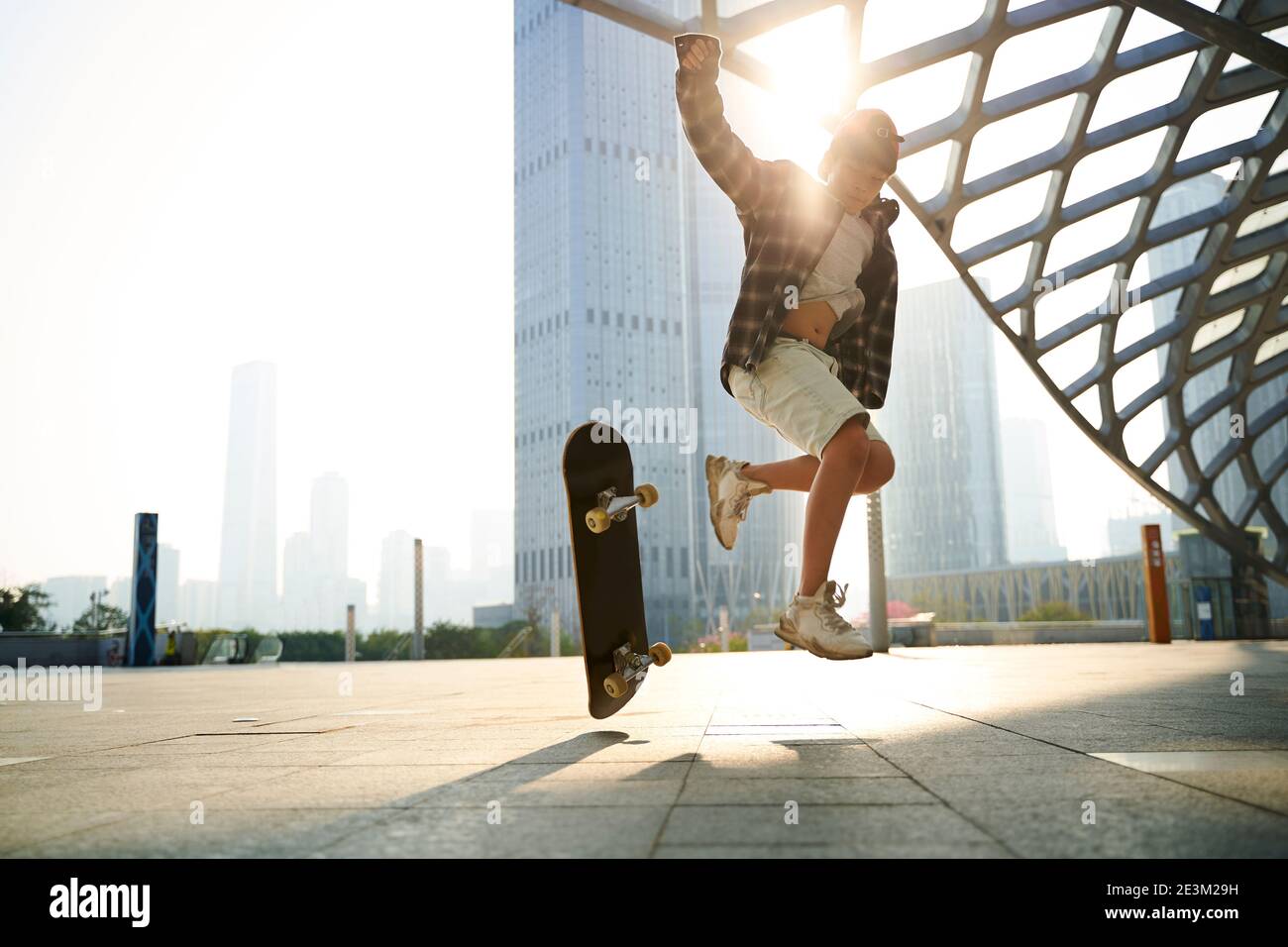Teenager asiatische Kind üben Skateboarding im Freien auf Stadtplatz mit Modernes Gebäude im Hintergrund Stockfoto