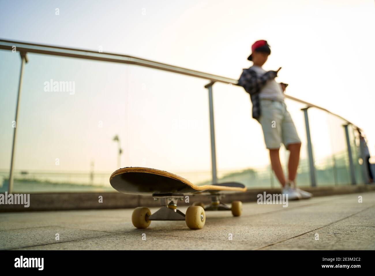 Teenage asiatische Skateboarder Junge Blick auf Handy während der Ruhe, konzentrieren Sie sich auf das Skateboard Stockfoto