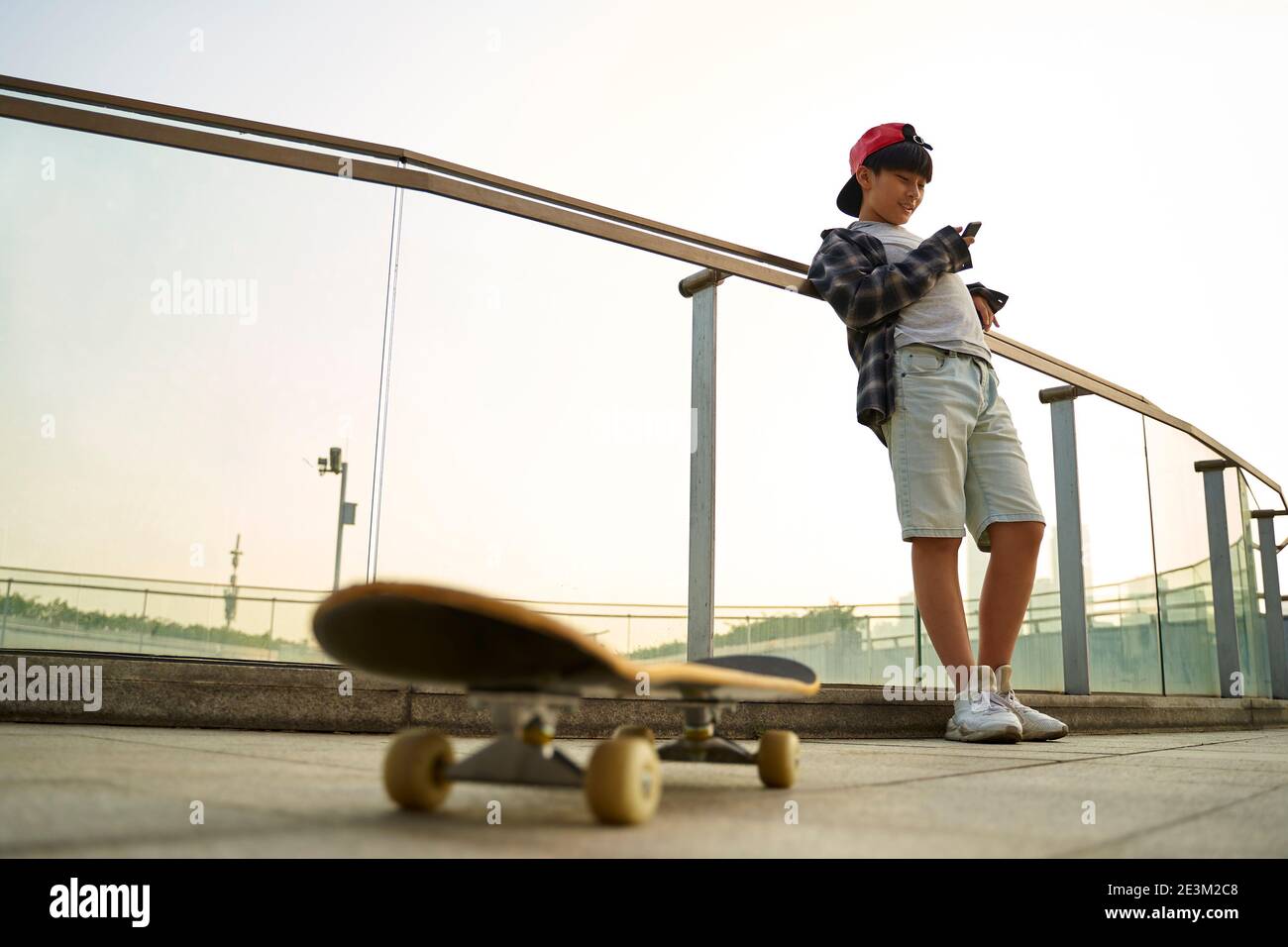Teenage asiatische Skateboarder Junge Blick auf Handy während der Ruhe Stockfoto
