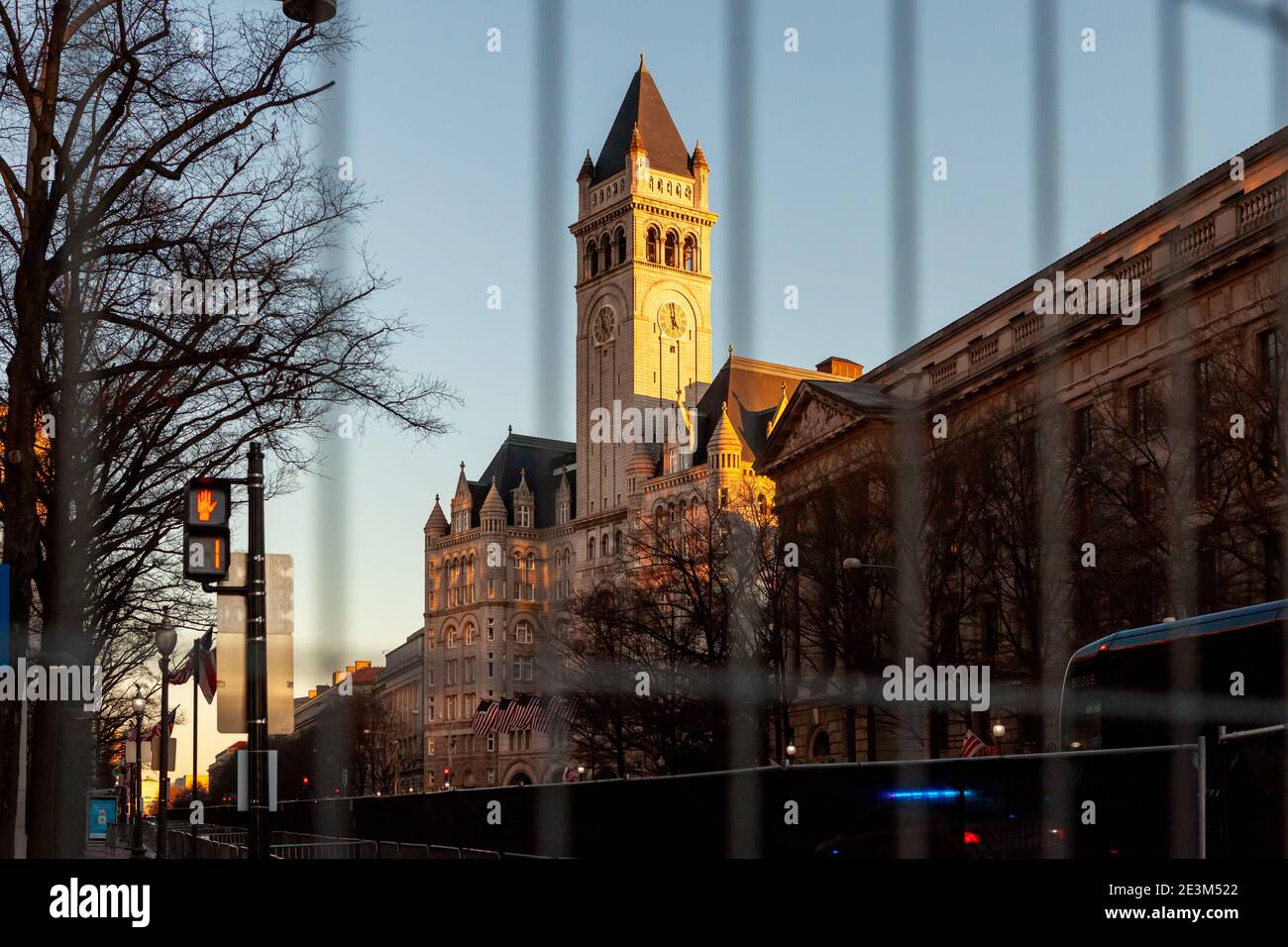 Washington, DC, USA, 19. Januar 2021. Im Bild: Der Turm des alten Postgebäudes, das heute das Trump Hotel ist, bei Sonnenuntergang durch den Sicherheitszaun gesehen. Die untergehende Sonne und eine Sekunde links auf dem Fußgängersignal schienen eine passende Metapher für die Trump-Regierung zu sein, die etwa 24 Stunden nach der Aufnahme des Fotos endet. Die Vorbereitungen und Sicherheitsmaßnahmen für die Amtseinführung von Joe Biden wurden viel früher als gewöhnlich eingeleitet, weil Trump-Anhänger, weiße VormachthaberInnen und andere Rechtsextremisten mit Gewalt drohten. Kredit: Allison C Bailey/Alamy Live Nachrichten Stockfoto