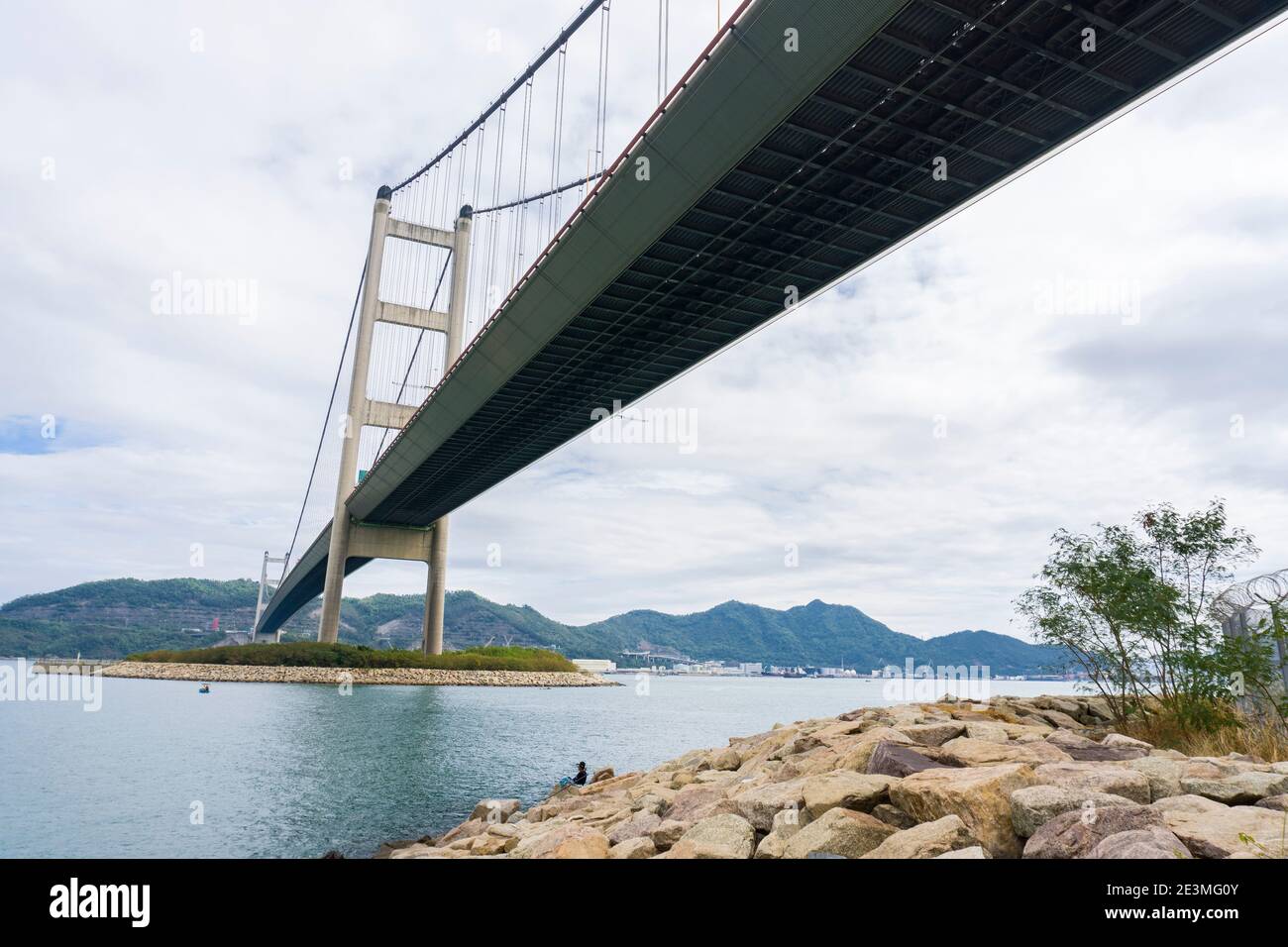 Tsing Ma Brücke zwischen Ma Wan Insel und Tsing Yi Insel. Eine Frau fischt unter der Brücke. Low-Angle-Ansicht Stockfoto