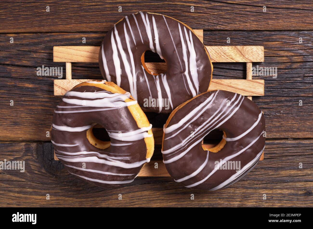 Drei Donuts mit Schokolade auf dunklem Holzplatte, Draufsicht Stockfoto