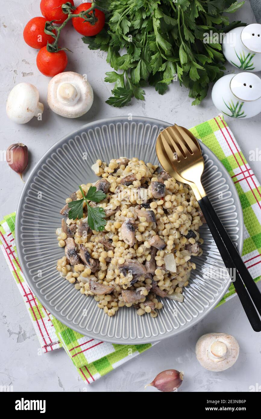 Hausgemachte Ptitim Pasta mit Champignons auf einem Teller auf hellgrauem Tisch. Vertikales Format. Blick von oben Stockfoto