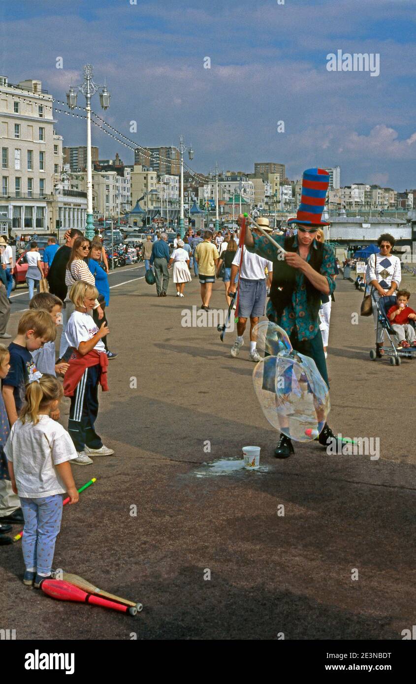 Ein Strandunterhalter, der 1996 auf der Promenade in der Nähe des Piers in Brighton, East Sussex, England, Großbritannien, riesige, zusammengeballte Blasen kreiert. Jemand, der in dieser Verfolgung engagiert wird, wird manchmal ein Bubbleologist genannt. Eine Seifenblase ist ein extrem dünner Film aus Seifenwasser, der Luft umschließt, die eine hohle Kugel mit einer irisierenden Oberfläche bildet. Sie können durch Blasen oder mit einer Blase ‘Zauberstab’ wie hier gemacht werden. Seifenblasen dauern normalerweise nur wenige Sekunden, bevor sie platzen, entweder allein oder bei Kontakt mit einem anderen Gegenstand. Dieser Entertainer hat auch Jonglierkünste – seine Clubs sind auf dem Boden um ihn herum. Stockfoto