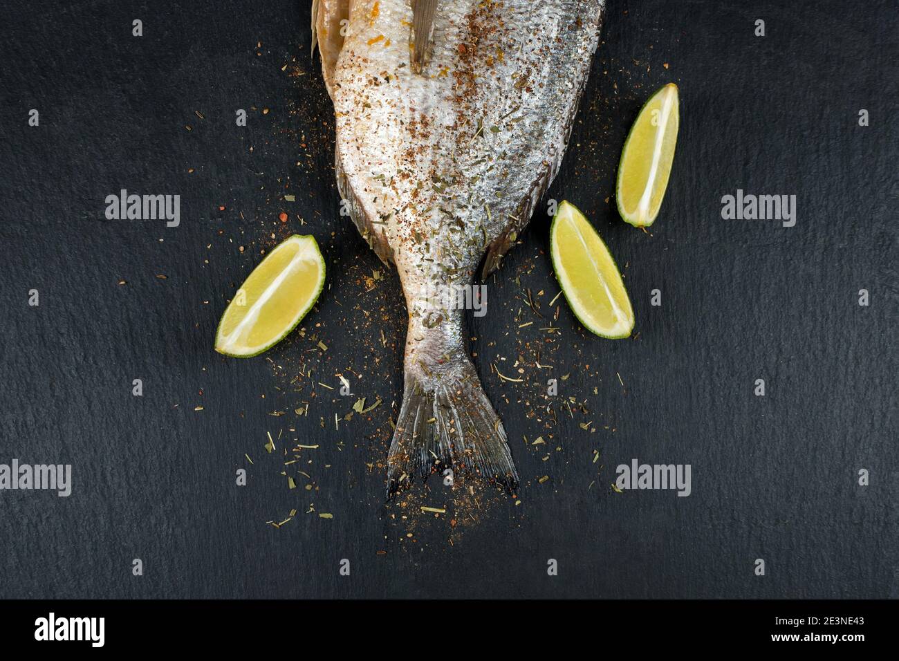 Schwanz von frischem rohem dorado auf schwarzem Schiefersteinbrett mit Gewürzen, Kräutern und Limette. Brassen Fisch bereit zum Kochen. Draufsicht. Stockfoto