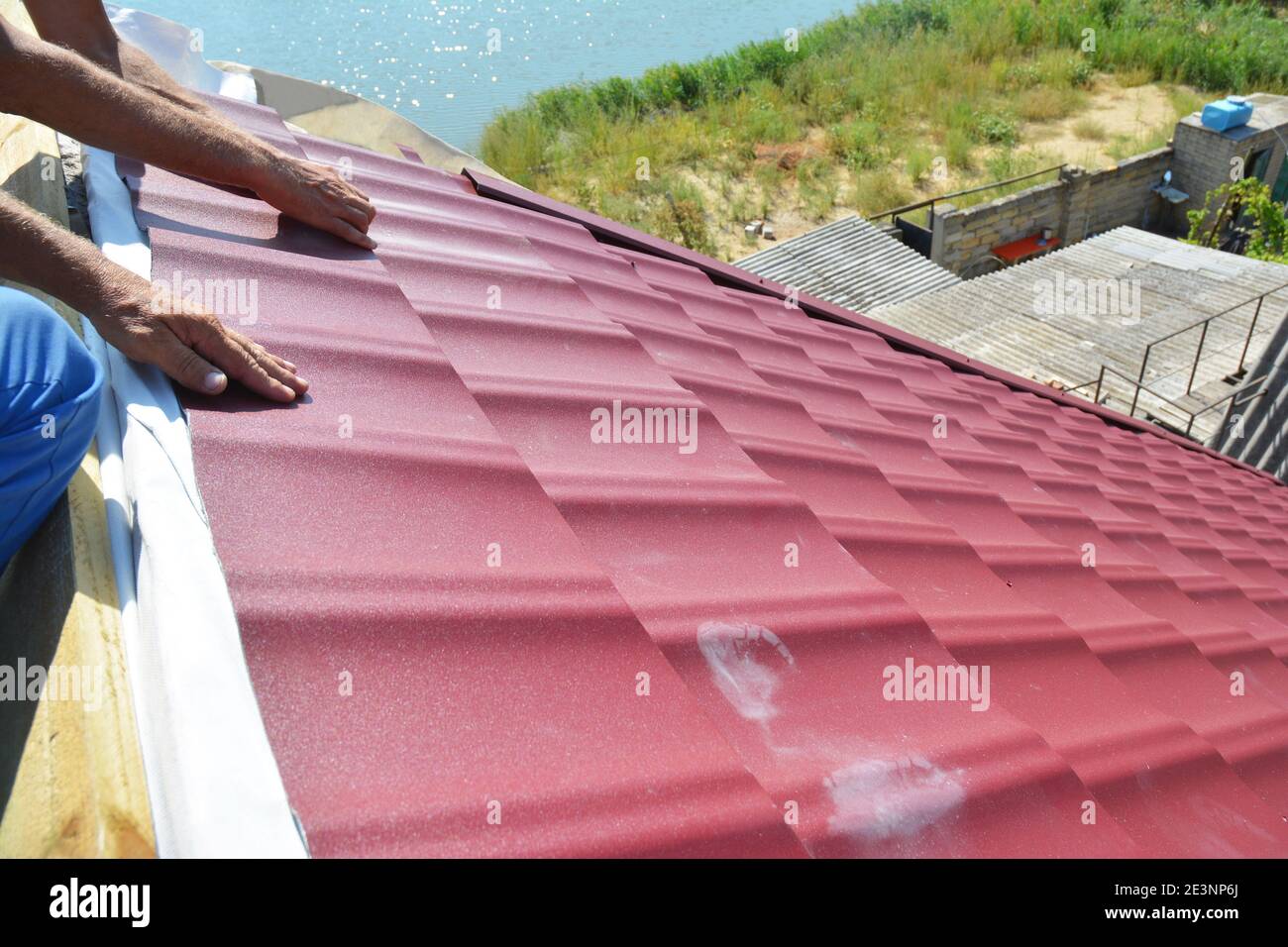 Dachkonstruktion. Ein Bauunternehmer installiert auf dem Dachrücken des Dachs Wellblechverkleidungen, Schilde und Dachzierleisten aus Rotmetall. Stockfoto