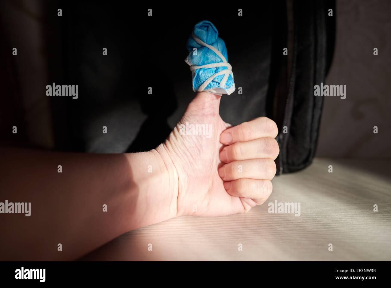 Weibliche Hand zeigt ok Schild. Der Daumen ist in einen Verband aus einer medizinischen Maske aus der Covid-Ära gewickelt. Stockfoto