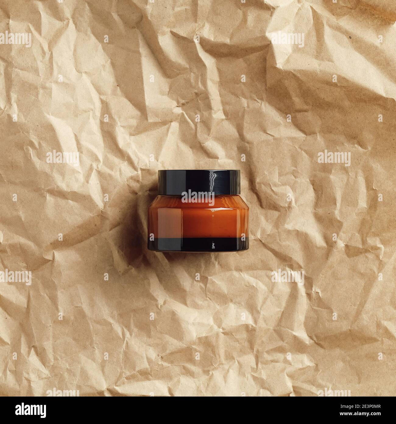 Natürliche feuchtigkeitsspendende Gesichtscreme in Bernstein Glas auf zerknittertem Papier, Draufsicht. Handgemachtes Branding für kosmetische Produkte Stockfoto