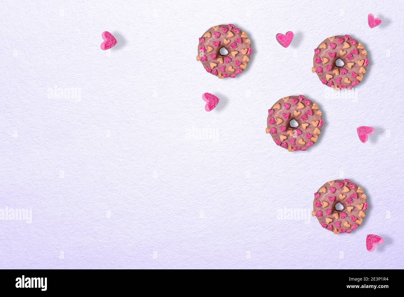 Drei leckere glasierte rosa Donuts mit Marshmallow Herzen. Nur wenige Herzen fliegen um Donuts herum. Texturierter Hintergrund aus lila Papier. Vorlage für Valen Stockfoto