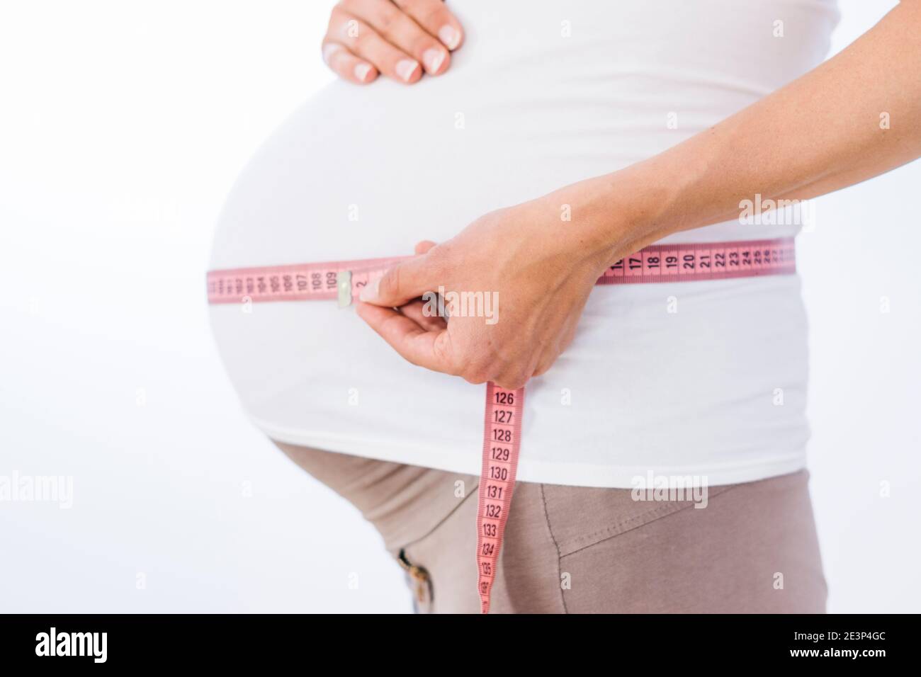 Schwangere Frau misst ihren großen Bauch auf weißem Hintergrund Stockfoto