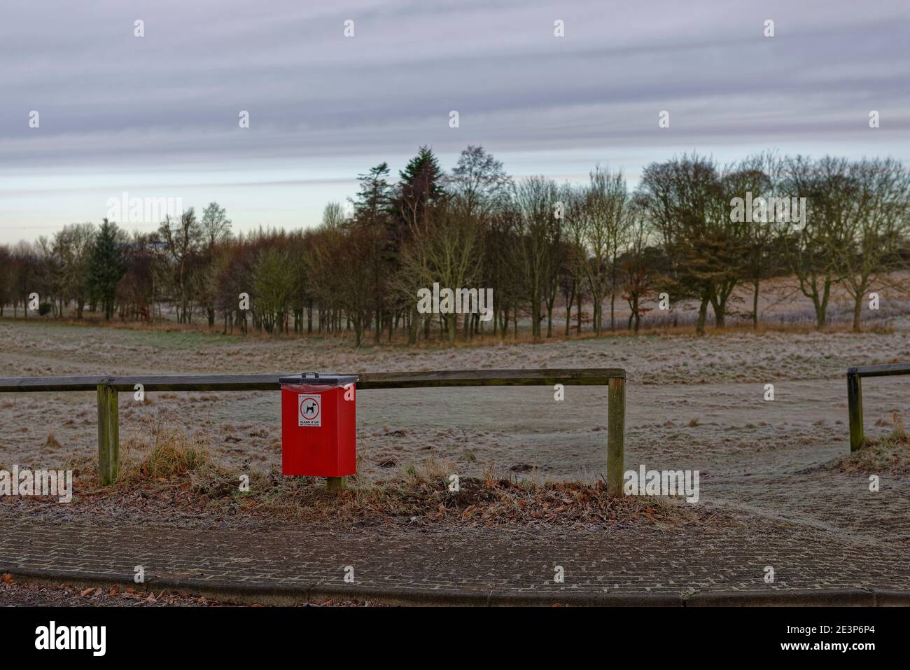 Eine rote Hundehüte mit Schild neben einem hölzernen Zaun Geländer, auf einem Bürgersteig bei einem Frosted Fairway des Letham Grange Golf Course. Stockfoto