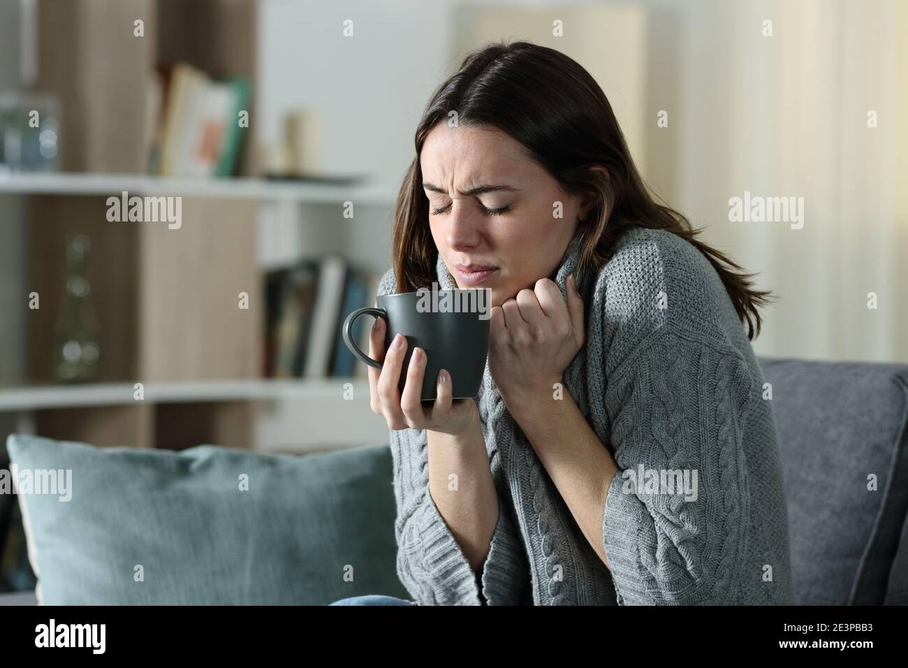 Wütend Frau immer kalt halten Kaffee Tasse und grabbing Pullover Sitzen auf einer Couch zu Hause Stockfoto