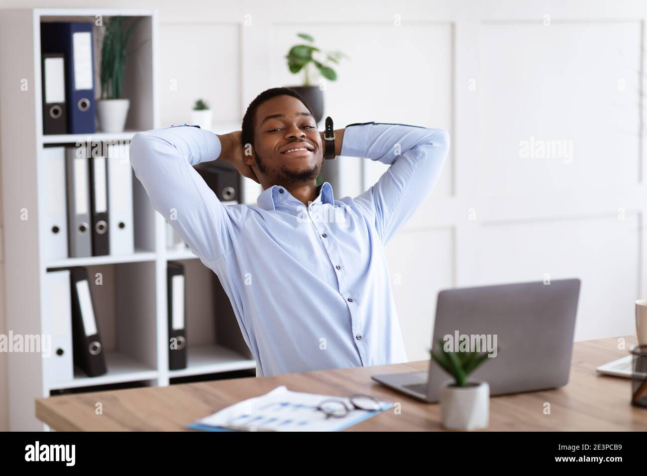 Glücklicher afroamerikanischer Mann, der im Büro auf seinem Stuhl ruht Stockfoto