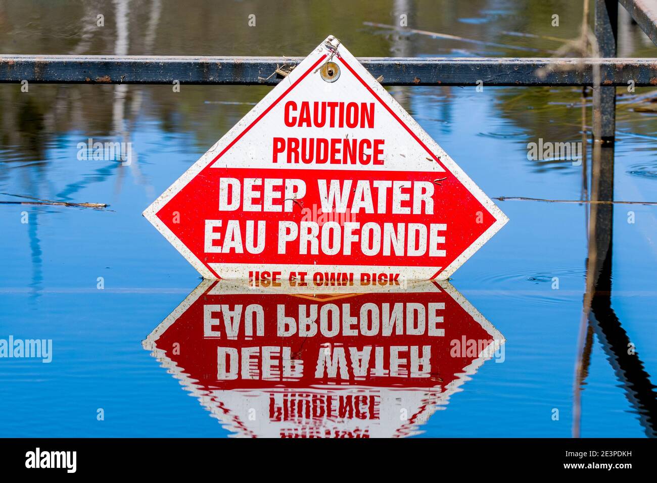 Schild Warnung vor tiefem Wasser. Teil des Zeichens ist untergetaucht. Sign ist in Englisch und Französisch. Reflexion des Zeichens ist im Wasser unten. Stockfoto