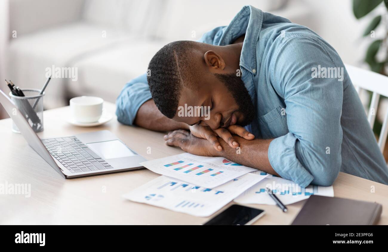 Schlafen Bei Der Arbeit. Erschöpfter schwarzer Freiberufler, der am Schreibtisch im Heimbüro nippt Stockfoto