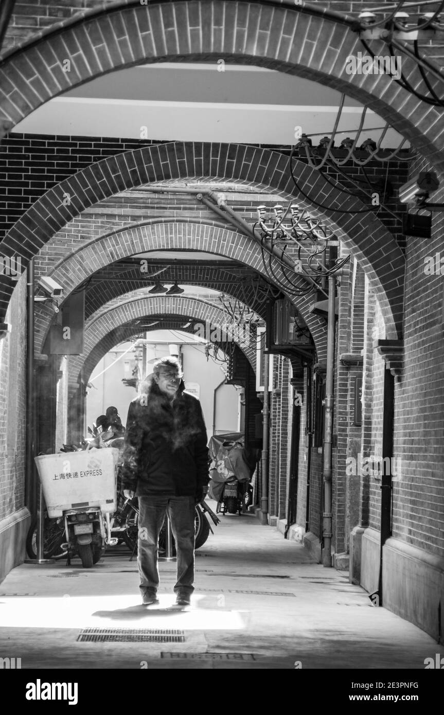 Ein alter Mann, der in einer Gasse traditioneller Shikumen-Häuser an der zentralen Huai Hai Road, einer der Haupteinkaufsstraßen in Shanghai, raucht. Stockfoto