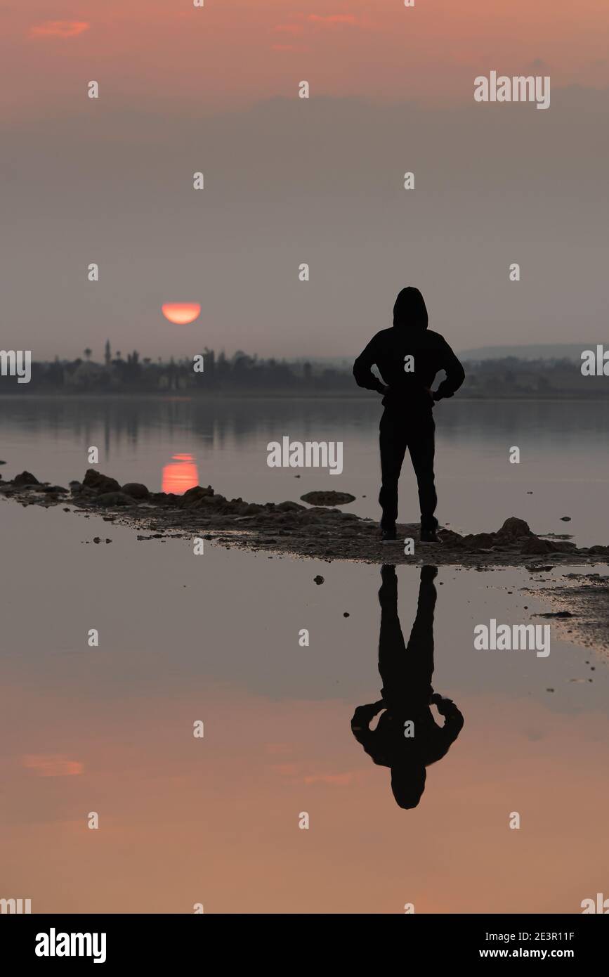 Unerkannte Person steht und genießt den Sonnenuntergang an einem See. Larnaka Zypern Stockfoto