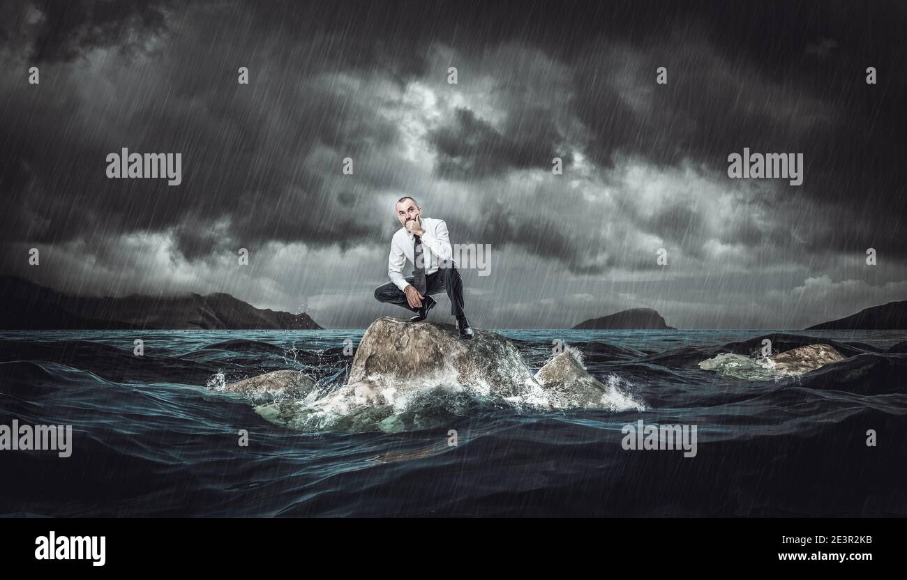 Nachdenklicher Mann auf einem Felsen im rauen Meer während eines Sturms. Konzept der Widrigkeiten und Probleme bei der Arbeit. Stockfoto