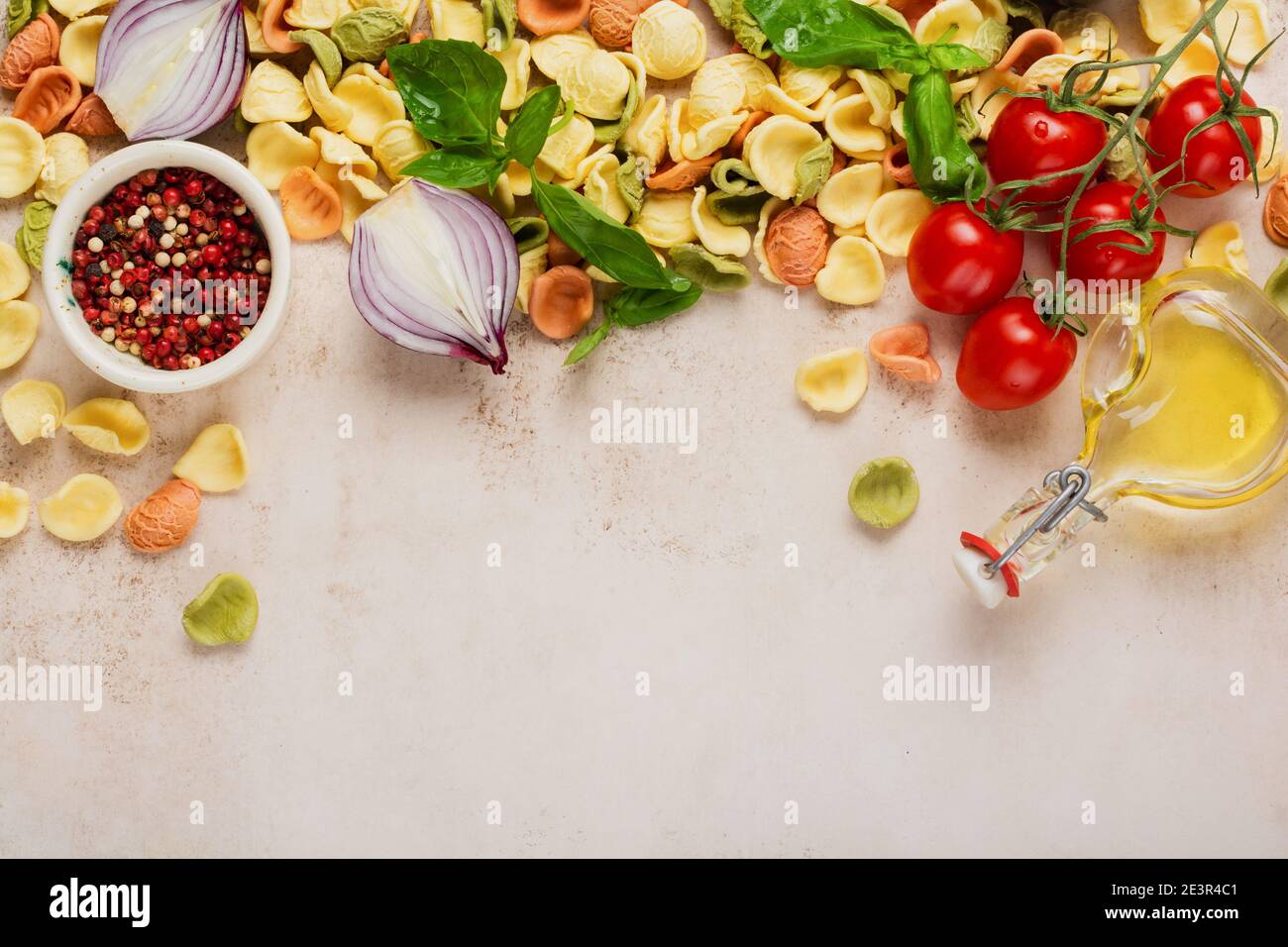 Rohe Orecchiette mit Parmesankäse und Tomaten, Basilikum, Knoblauch und Öl auf hellem Hintergrund mit Pfeffer auf hellbraunem Hintergrund. Traditionell eingetellt Stockfoto