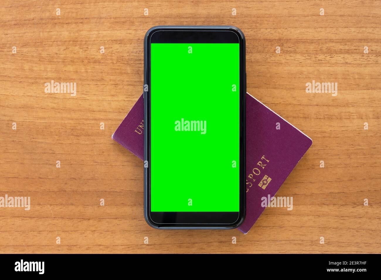 (Selektiver Fokus) AUF einem Holztisch SIND EIN Reisepass und ein Smartphone mit grünem Bildschirm angeordnet. Reisekonzept mit Kopierplatz. Stockfoto