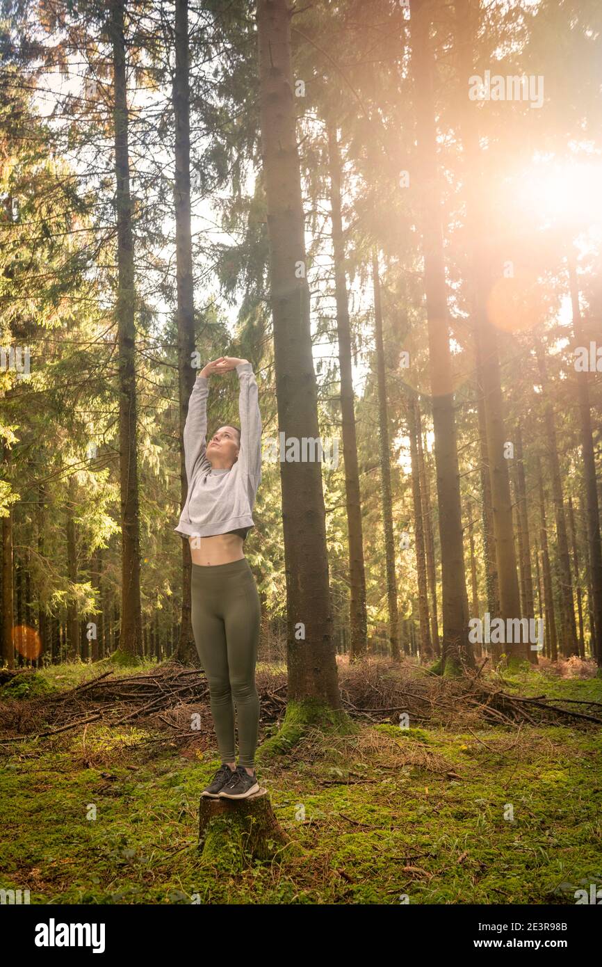 Frau, die Arme streckt und frische Luft mitten im Wald atmet, während sie bei Sonnenaufgang trainiert. Workouts und Lifestyle-Konzept. Stockfoto