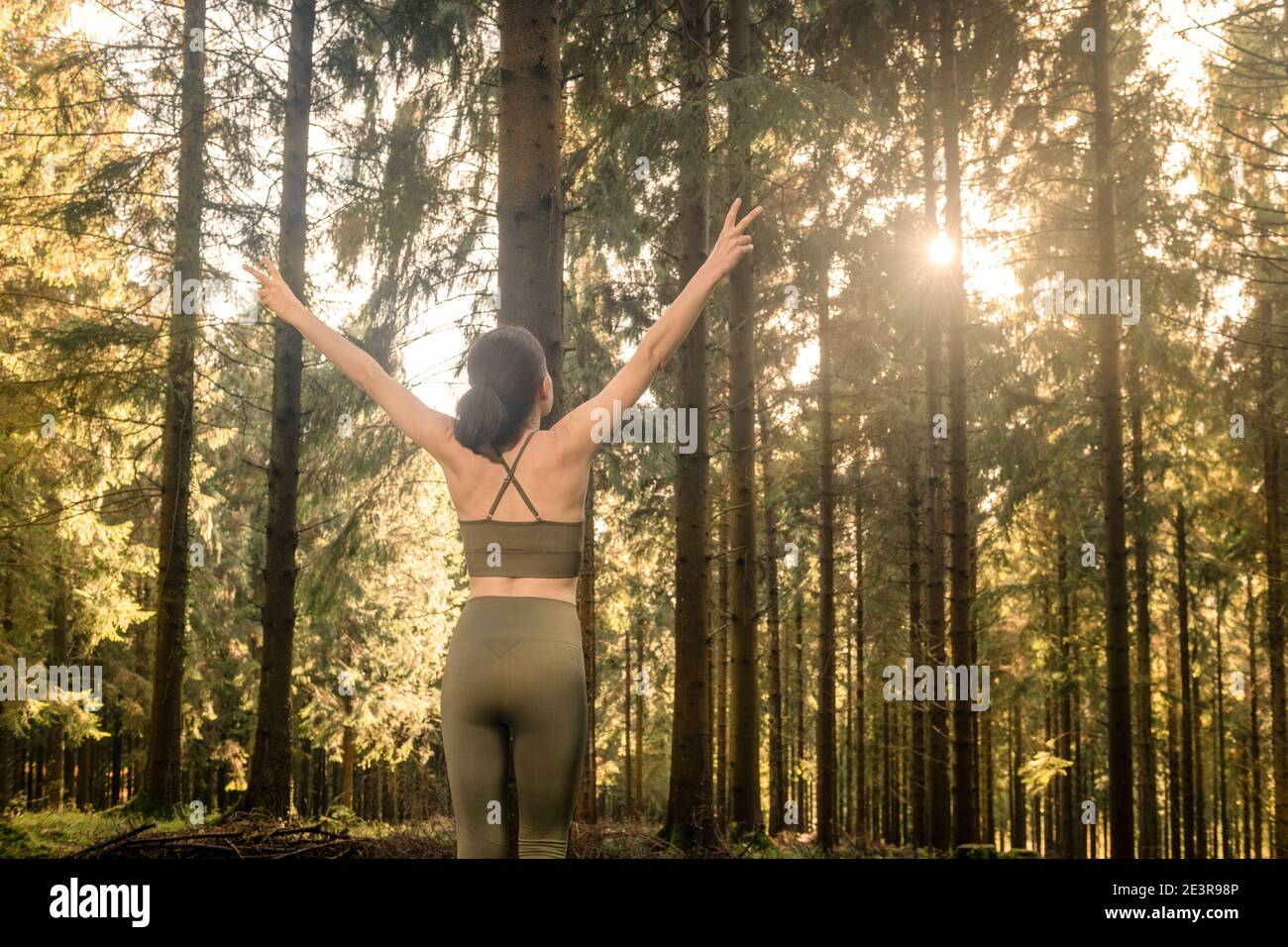 Frau, die Arme streckt und frische Luft mitten im Wald atmet, während sie bei Sonnenaufgang trainiert. Workouts und Lifestyle-Konzept. Stockfoto