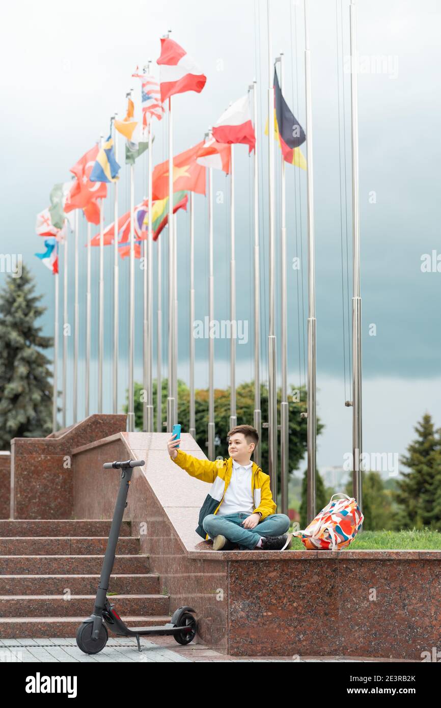 Teenager sitzt in der Nähe des Verwaltungsgebäudes vor dem Hintergrund der Länderflaggen Und spricht über Videoanruf Stockfoto