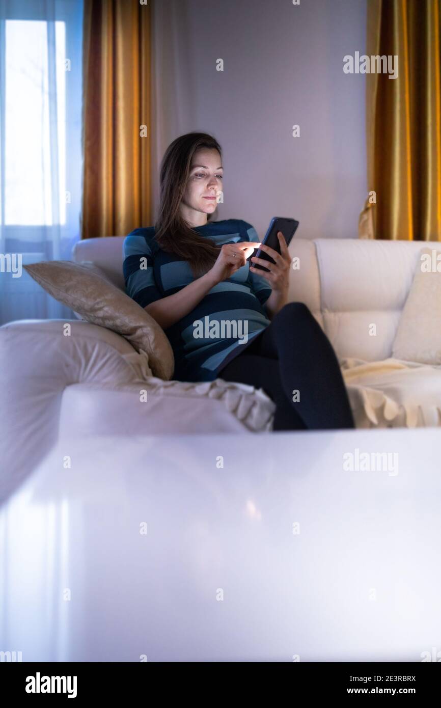 Frau browsing ihr Smartphone in ihrer gemütlichen Wohnung während der Abend Stockfoto