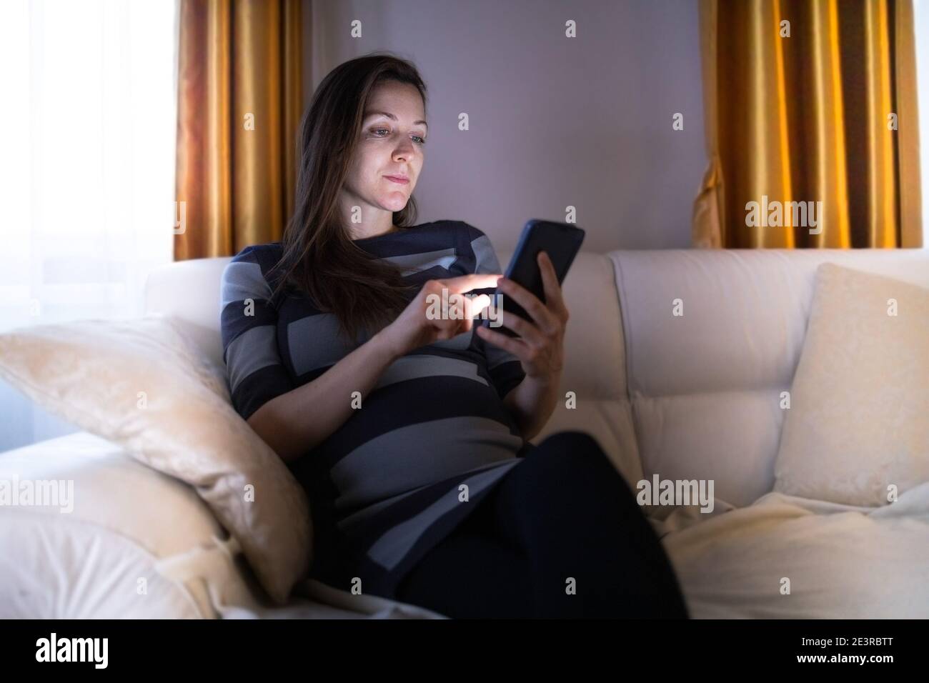 Frau browsing ihr Smartphone in ihrer gemütlichen Wohnung während der Abend Stockfoto