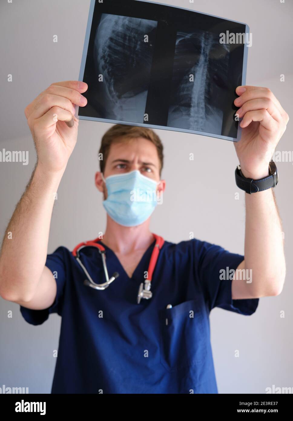 Ein hübscher Arzt, der Peeling, Stethoskop und Gesichtsmaske trug und während der sars COV 2 Pandemie Covid 19 auf eine Röntgenaufnahme blickte Stockfoto