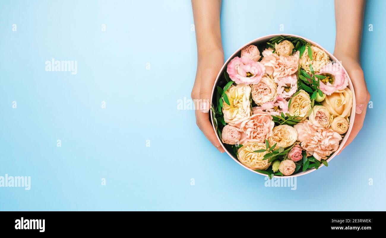 Florist hält einen Hut runde Box mit floralen Komposition auf einem blauen Hintergrund mit Kopierraum. Geschenkbox für 8. März, Valentinstag, Muttertag Stockfoto