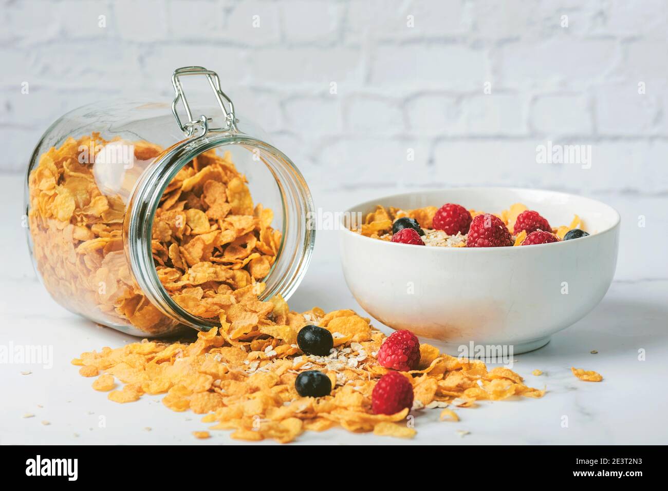 Gesundes Frühstück.Glas mit Getreide neben einer Schüssel Müsli, Cerealien, Himbeeren und Heidelbeeren auf Marmortisch Stockfoto