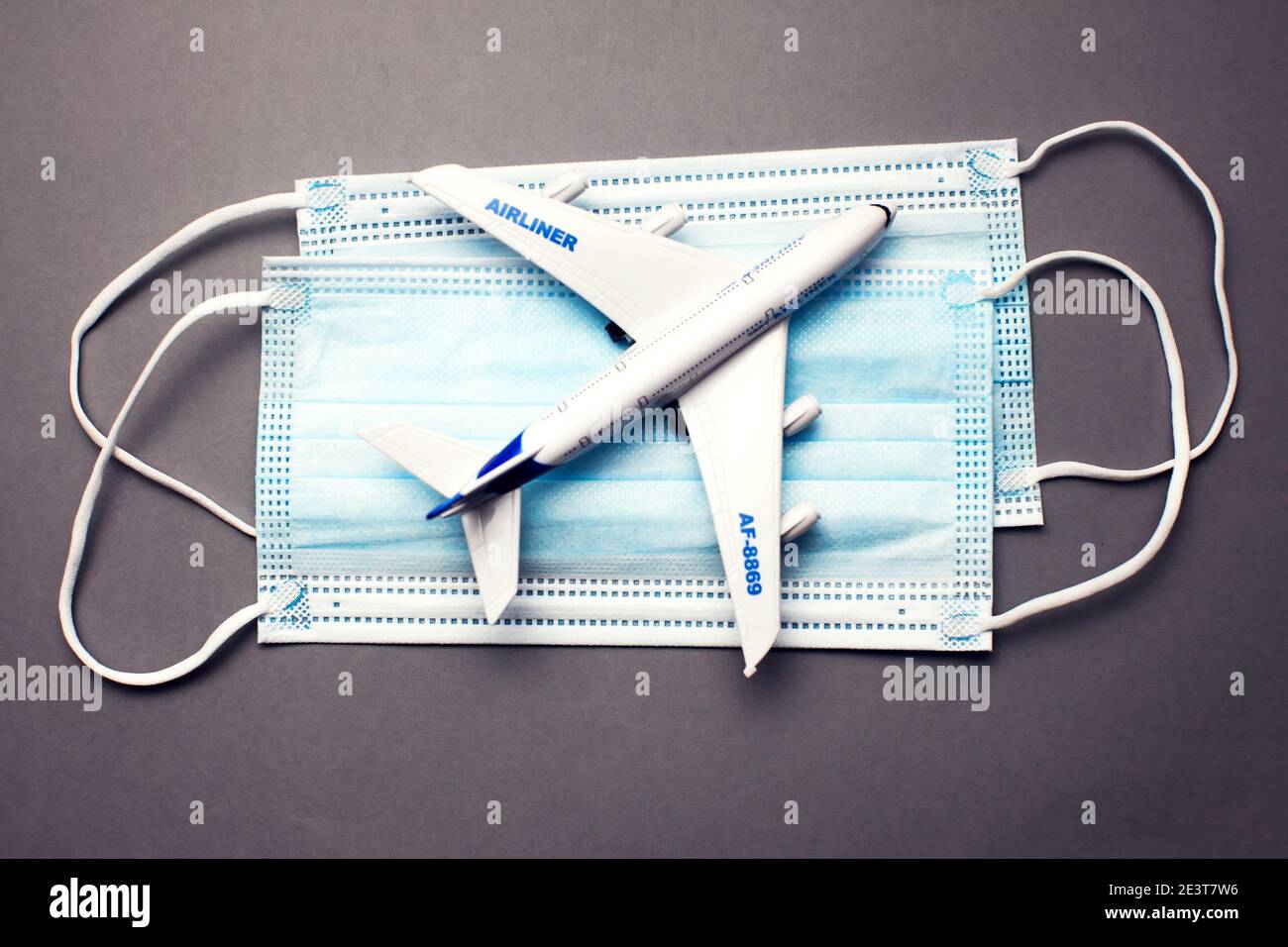 Reise- und Gesundheitskonzept während der covid-19-Pandemie. Modell eines weißen Plastikflugzeugs und Masken auf grauem Hintergrund. Stockfoto