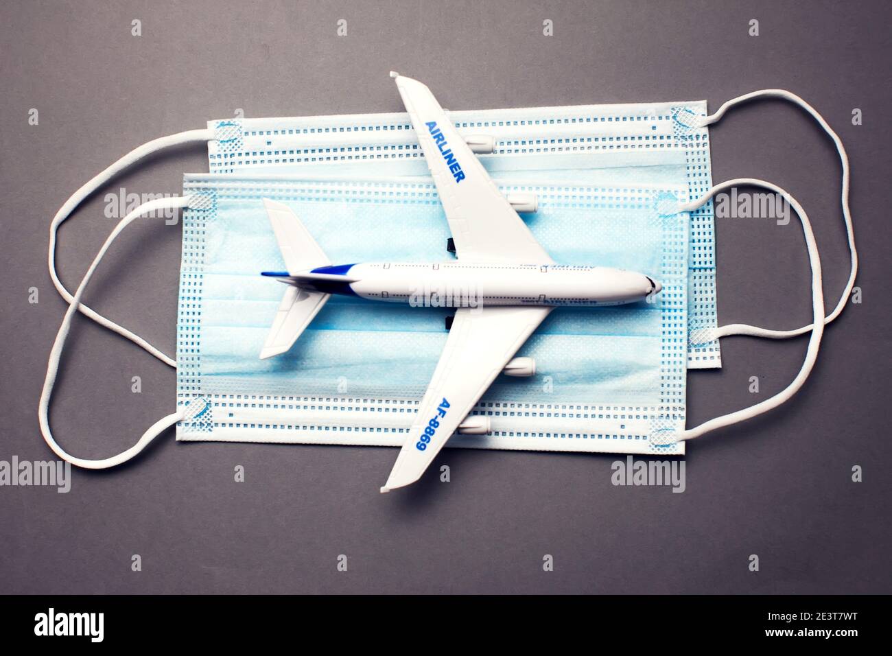 Reise- und Gesundheitskonzept während der covid-19-Pandemie. Modell eines weißen Plastikflugzeugs und Masken auf grauem Hintergrund. Stockfoto
