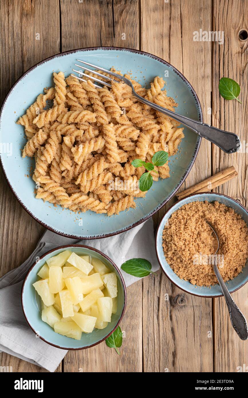 Einfache Fusilli-Pasta mit süß gebratenem Grieß und Zimt, serviert mit Ananasstücken Stockfoto