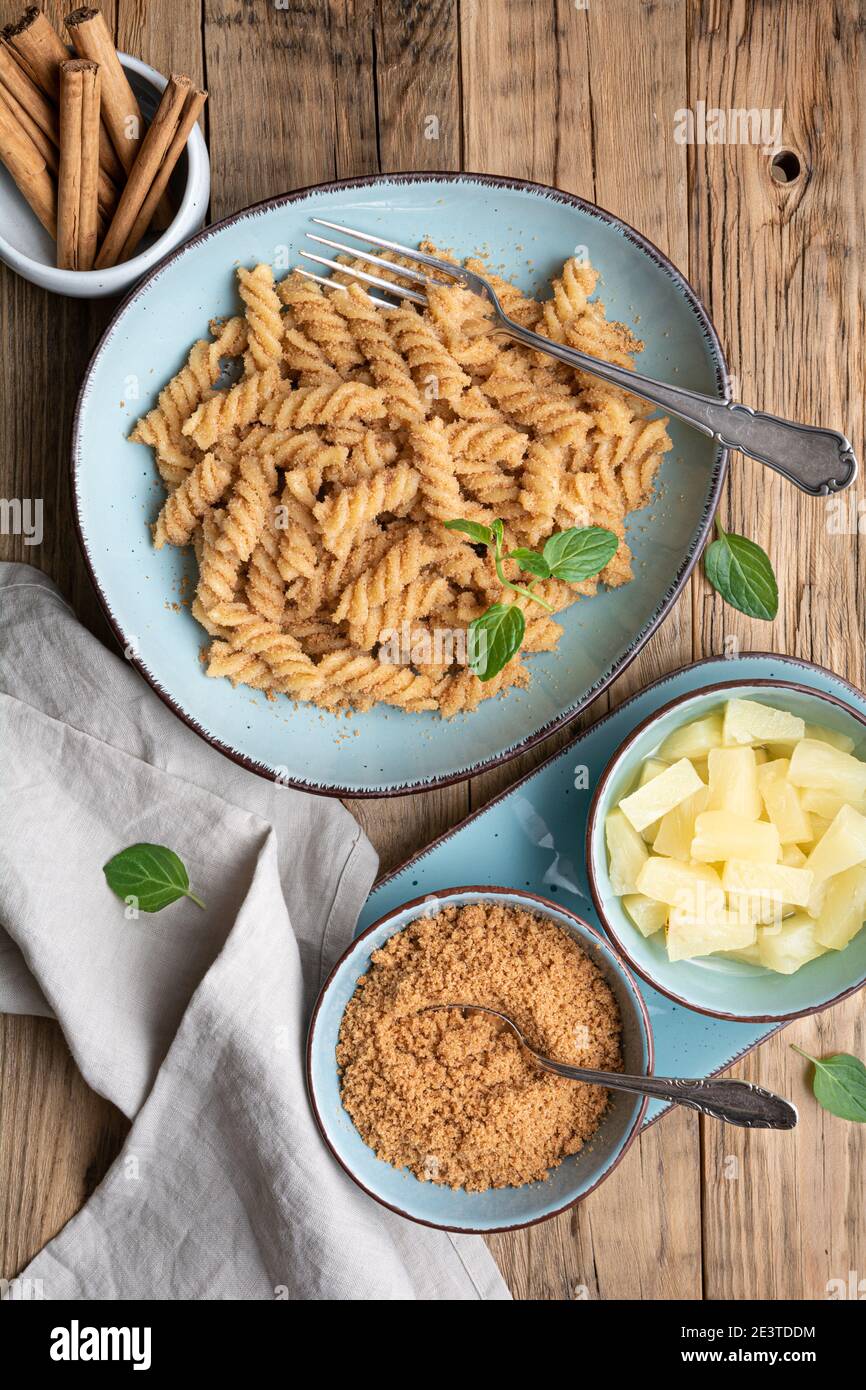 Einfache Fusilli-Pasta mit süß gebratenem Grieß und Zimt, serviert mit Ananasstücken Stockfoto