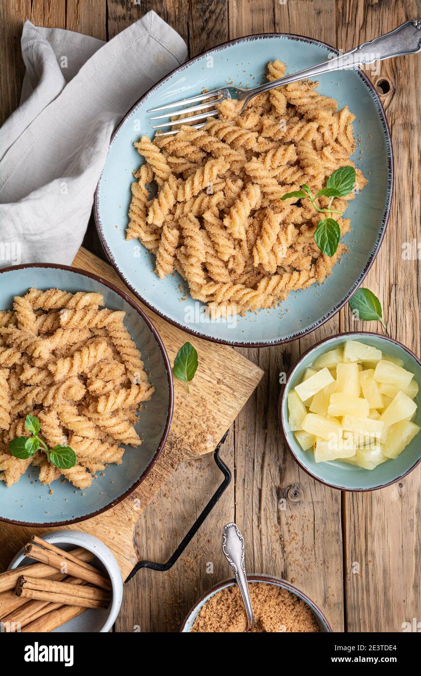 Einfache Fusilli-Pasta mit süß gebratenem Grieß und Zimt, serviert mit Ananasstücken Stockfoto