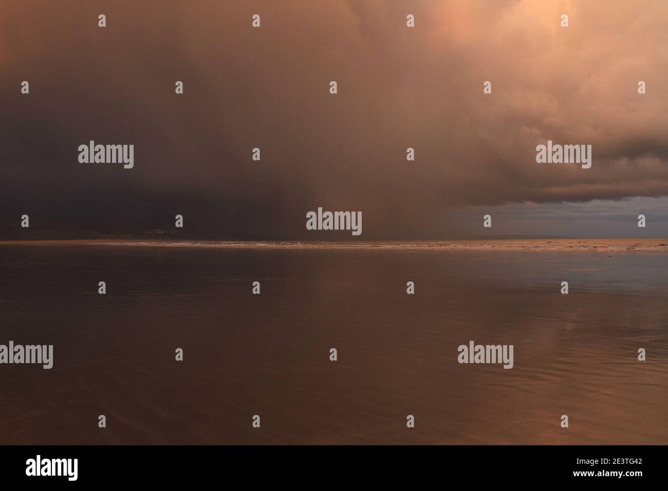 Storm Cloud bewegt sich am Black Rock Sands über den Strand und erzeugt einen dramatischen Himmel, wobei orange graue Wolken eine unheimliche Szene erzeugen Stockfoto
