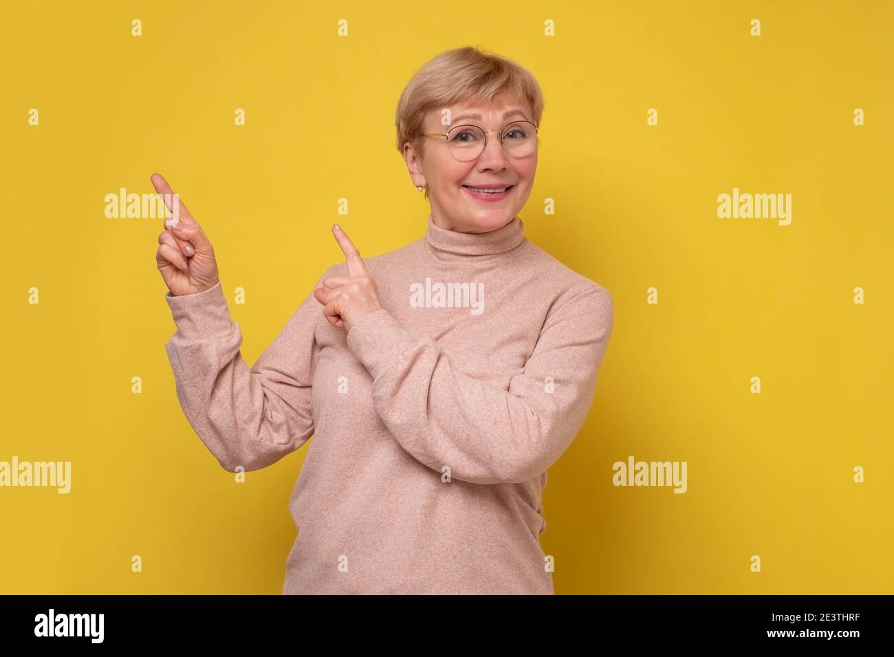Erstaunt aufgeregt reifen alten Frau zeigt auf Kopie Raum beiseite. Glücklich reife Dame Blick auf Kamera Werbung Produkt. Studioaufnahme Stockfoto