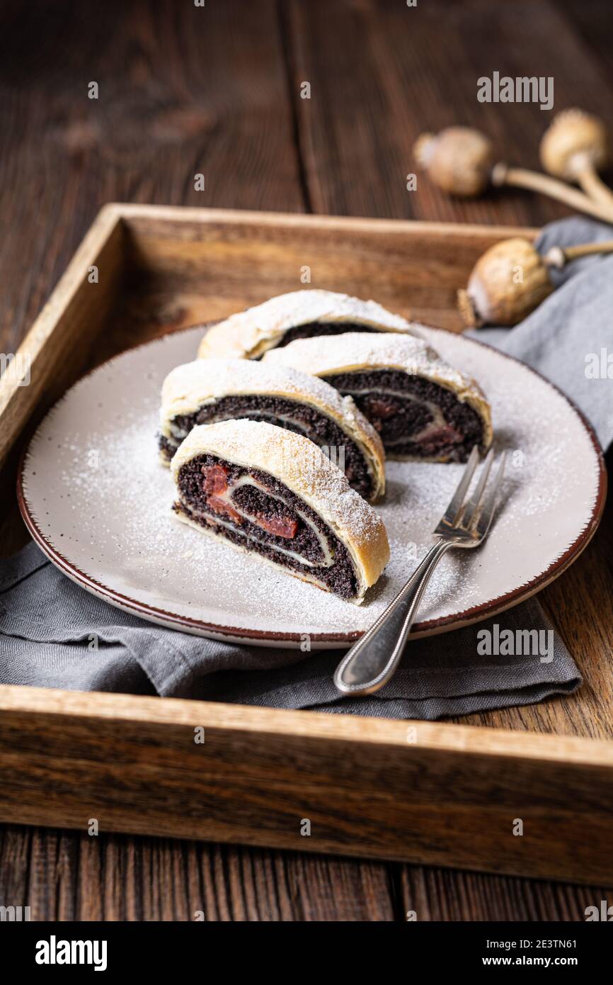 Köstliche gerollte Dessert, Blätterteig Mohn Strudel Scheiben mit Sauerkirsche, mit Puderzucker auf rustikalem Holzhintergrund bestäubt Stockfoto