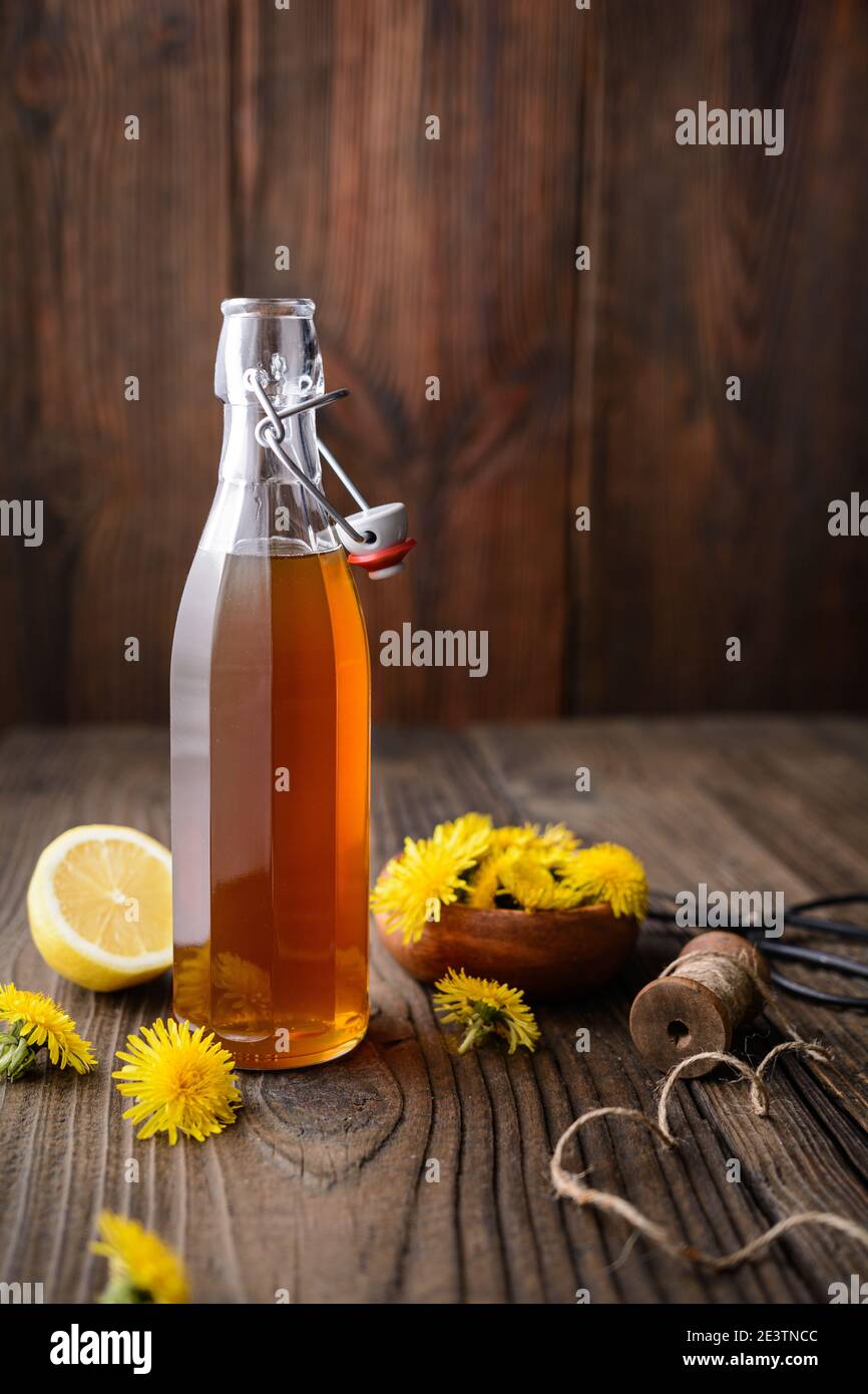 Hausgemachter gesunder Löwenzahn-Sirup in einer Glasflasche, dekoriert mit frischen Blumen auf rustikalem Holzhintergrund mit Kopierraum Stockfoto