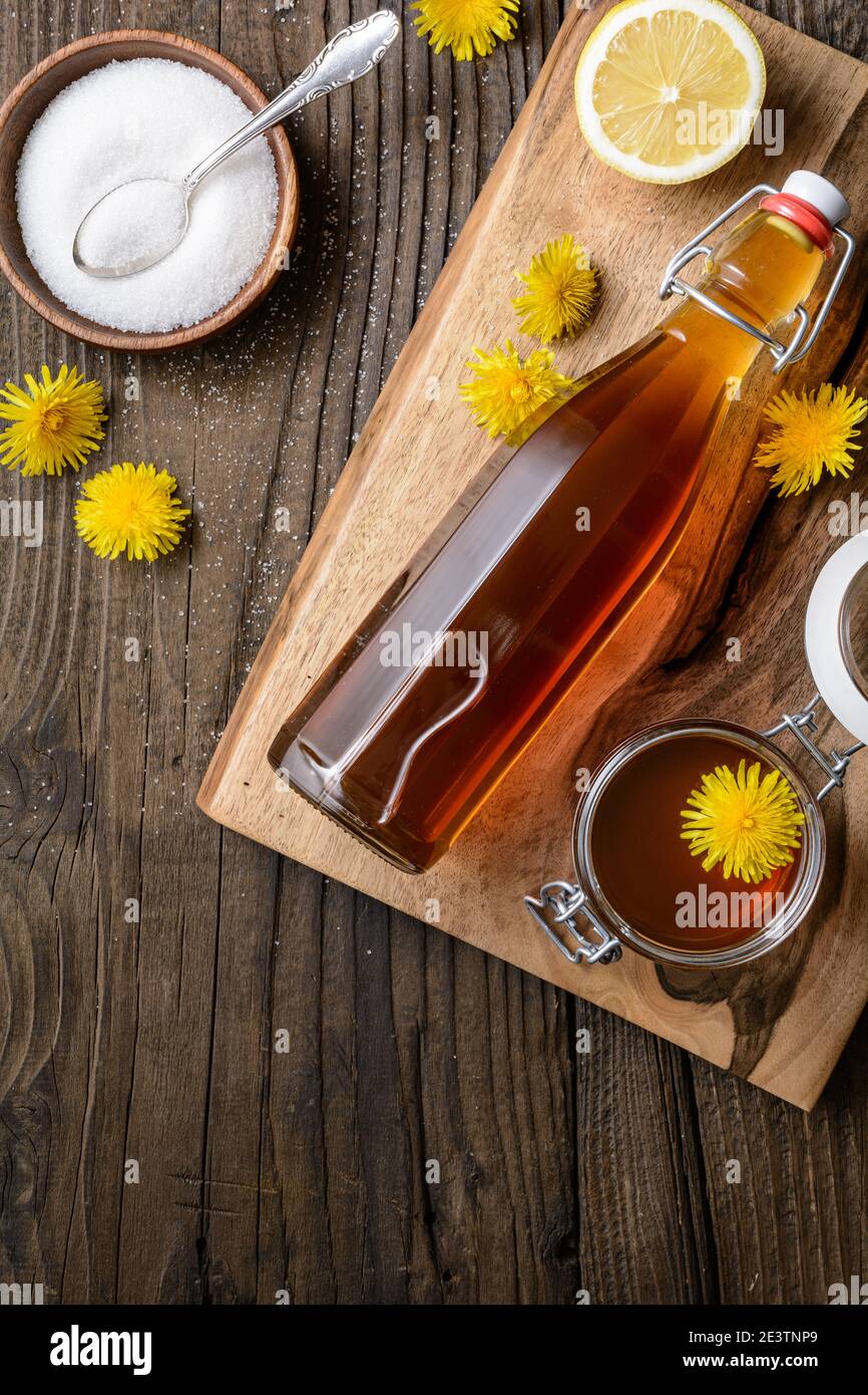 Hausgemachter gesunder Löwenzahn-Sirup in einer Glasflasche, dekoriert mit frischen Blumen auf rustikalem Holzhintergrund Stockfoto