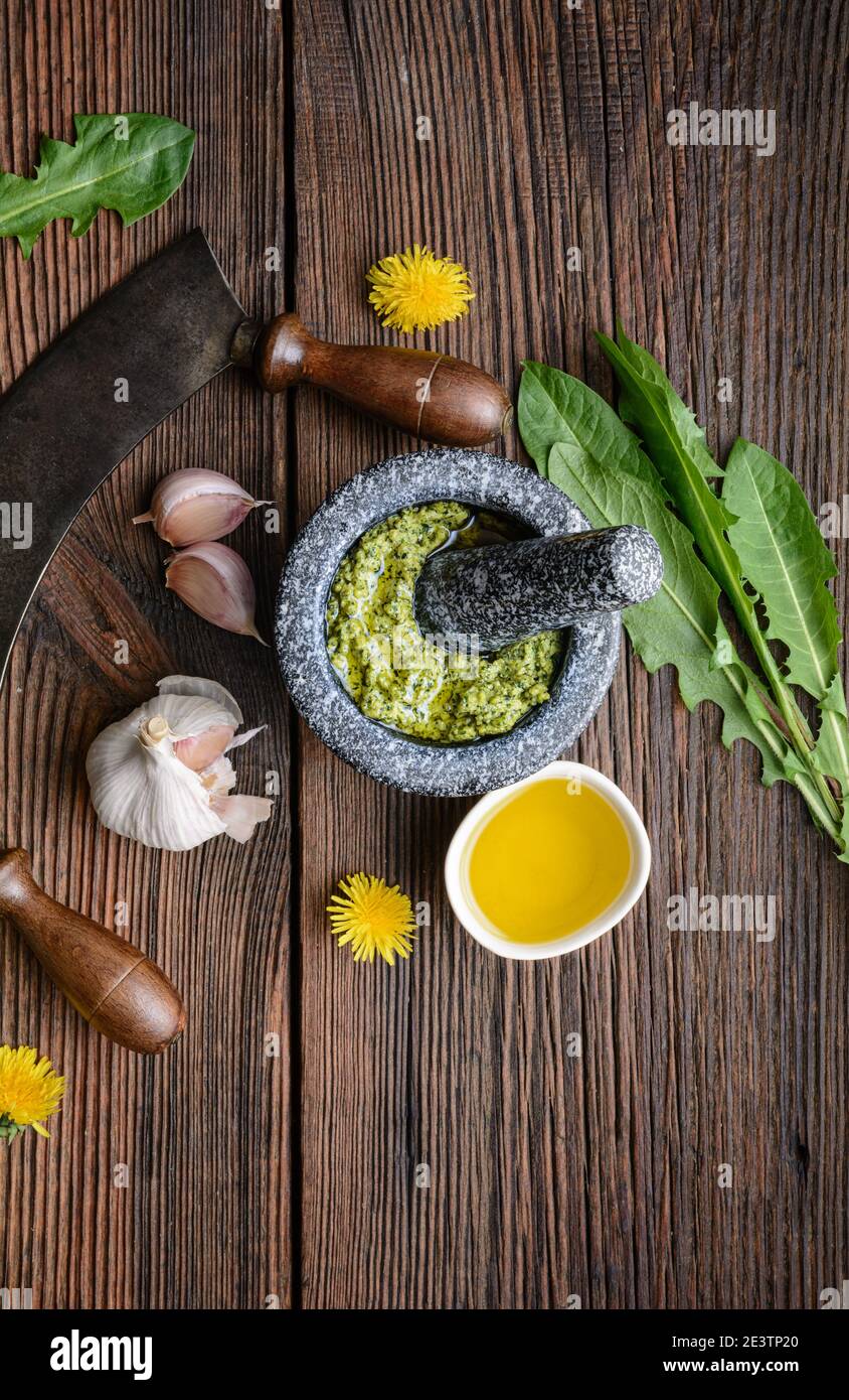 Gesundes Löwenzahn-Pesto mit Mandeln, Knoblauch, Olivenöl und Parmesankäse im Steinmörtel auf rustikalem Holzhintergrund Stockfoto