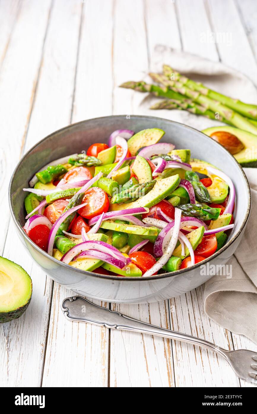 Gesundes veganes Gericht, saftiger Sommersalat mit blanchierten Spargel, Kirschtomaten, Avocado-Scheiben und roter Zwiebel, mit Pfeffer bestreut und mit Nieselteich beträufelt Stockfoto