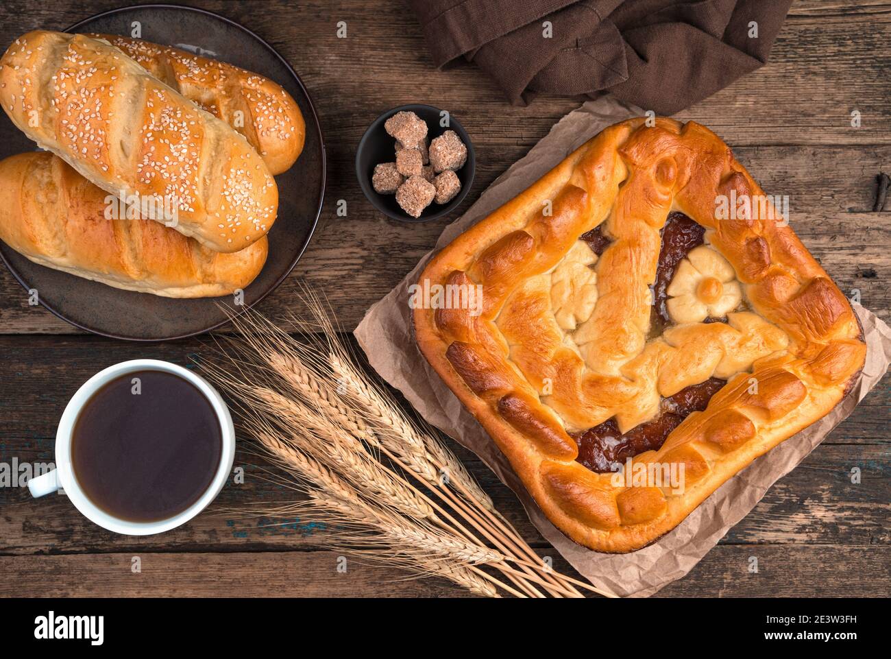 Apfelkuchen, frische Brötchen und Weizenspikeletts und eine Tasse Tee auf braunem Holzhintergrund. Stockfoto